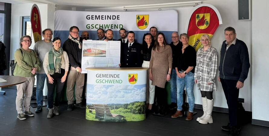 Eine Gruppe von Menschen bestenden aus Vertretern des Gemeinderats, Mitarbeiter des Rathaus Gschwend und Bürgermeister Ziehr steht lächelnd zusammen vor einem Hintergrund mit der Aufschrift "Gemeinde Gschwend" und einer Fahne. Einige halten ein Plakat mit dem Bild des neuen Feuerwehrhaus hoch. Eine Gruppe von Menschen bestenden aus Vertretern des Gemeinderats, Mitarbeiter des Rathaus Gschwend und Bürgermeister Ziehr steht lächelnd zusammen vor einem Hintergrund mit der Aufschrift "Gemeinde Gschwend" und einer Fahne. Einige halten ein Plakat mit dem Bild des neuen Feuerwehrhaus hoch.