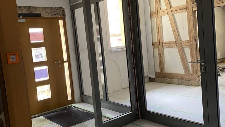 Dieser Raum befindet sich in einer Renovierung und zeigt zwei Doppeltüren mit Glaseinsätzen sowie teilweise freiliegende Wandstrukturen.